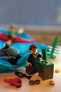 Lego figure holding briefcase in one hand and money in the other. There is a dolphin, lobster and fish covered in oil in the background.